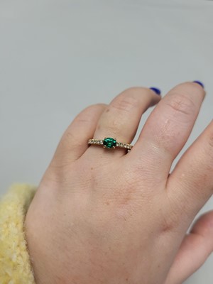 Lot 61 - AN EMERALD AND DIAMOND SET BAND RING, the oval...